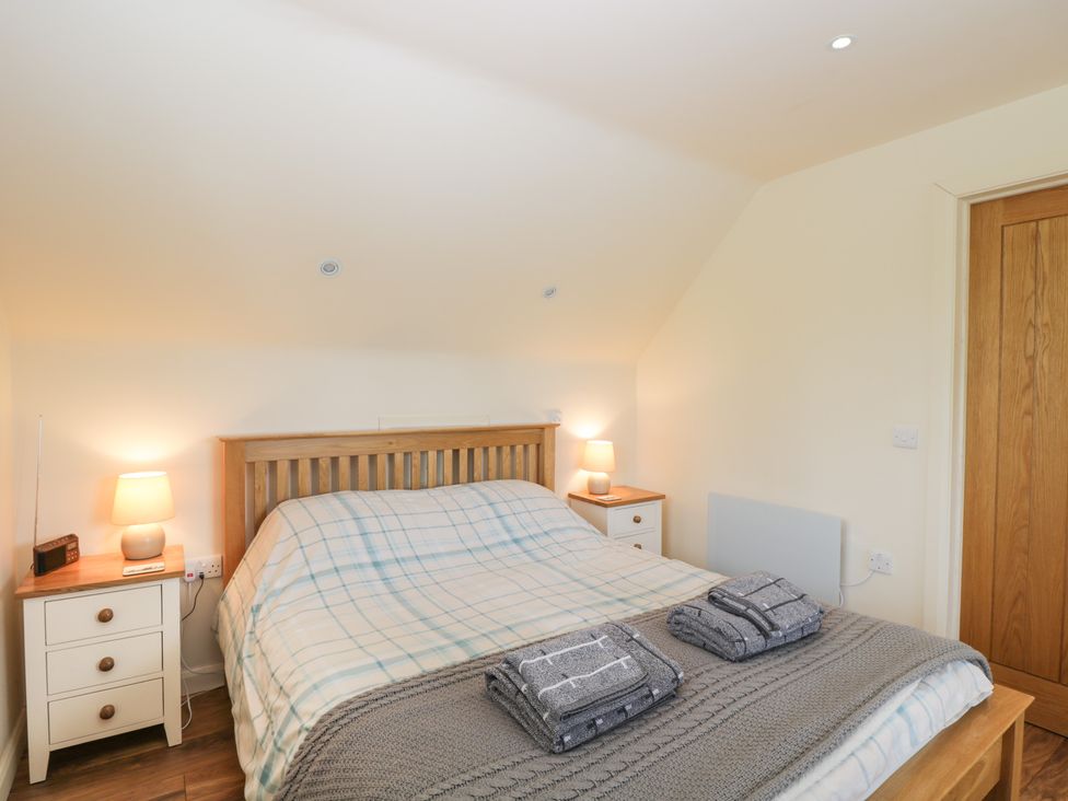 A bedroom with a wooden bed frame two bedside tables with lamps and folded towels on the bed at Shephard's Retreat in Charlton Mackrell near Somerton