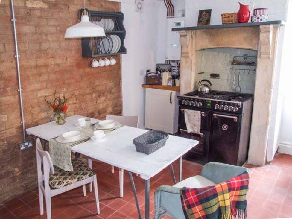 A kitchen with a white table set with dishes a brick wall a stove and chairs with a blanket at Woodland Cottage in Malvern