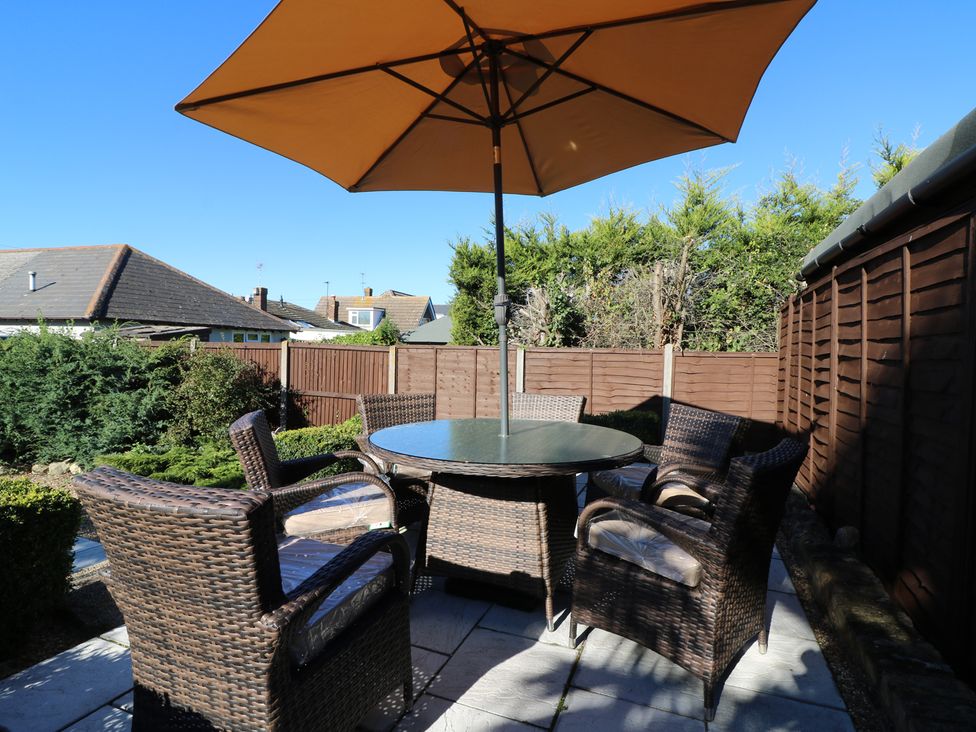 An outdoor patio area with a round glass table and six wicker chairs under a large brown umbrella at Smallcroft in Seasalter