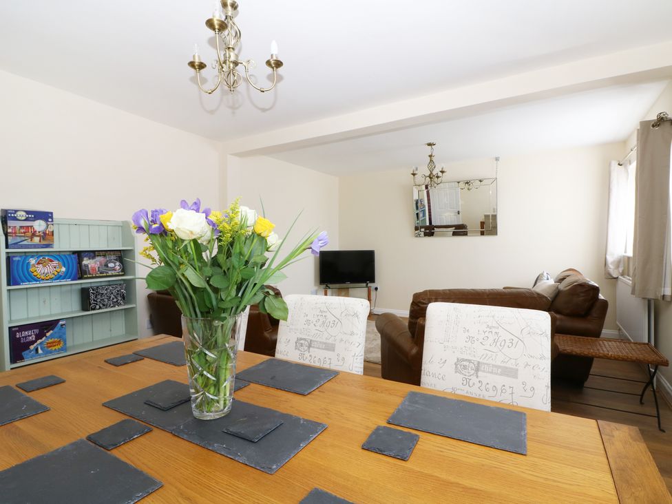 A dining table with a vase of flowers and placemats with chairs and a living area with sofas a television and a mirror at Smallcroft in Seasalter