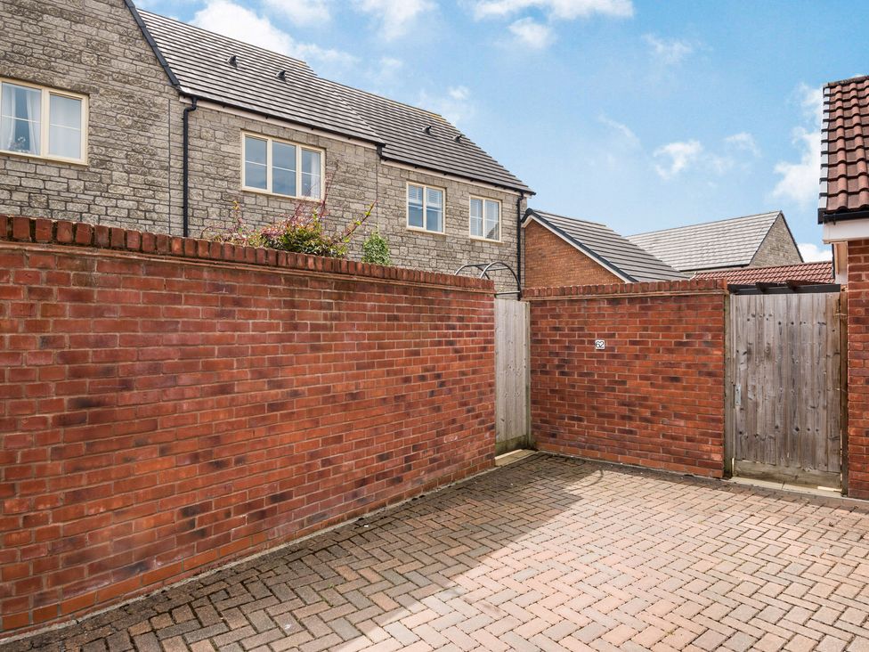 A brick-walled courtyard with a wooden gate and residential houses in the background at Saplings in Wells