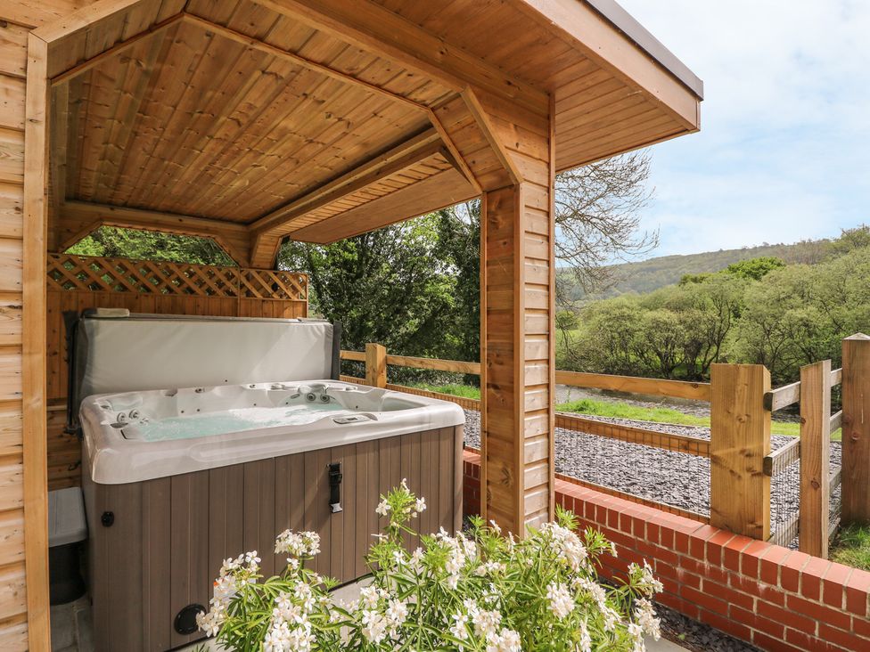 A covered outdoor hot tub with flowers in front and trees in the background at The Farmhouse in Capel Bangor near Aberystwyth