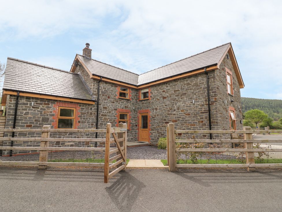 A stone house with wooden framed windows and a wooden gate in front at The Farmhouse in Capel Bangor near Aberystwyth