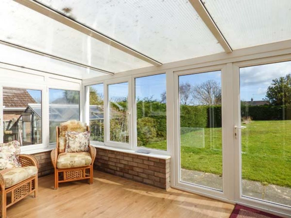 A sunroom with two wicker armchairs with cushions and glass doors opening to a garden at Skylark in Weybourne