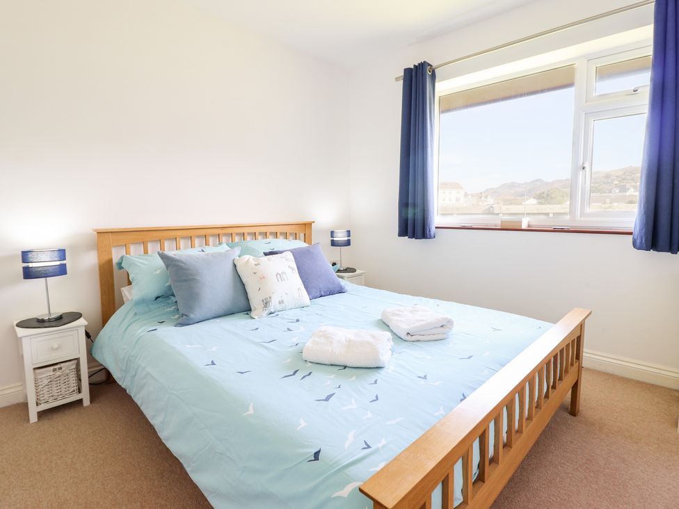 A bedroom with a wooden bed blue bedspread pillows bedside tables and a window with blue curtains at Sealyons Fairbourne near Dolgellau