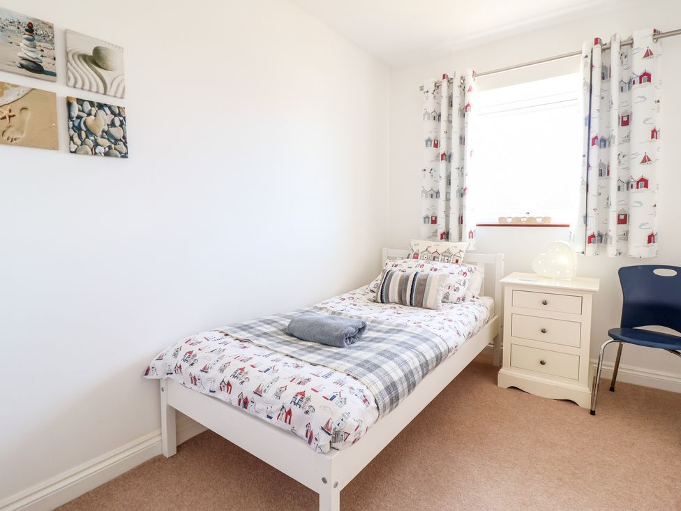 A bedroom with a single bed a bedside cabinet a chair and a window with curtains at Sealyons Fairbourne near Dolgellau