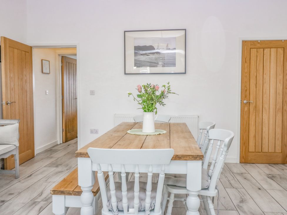 A dining room with a wooden table and white chairs with flowers in a vase on the table at Driftwood 23 Roa Island in Roa Island