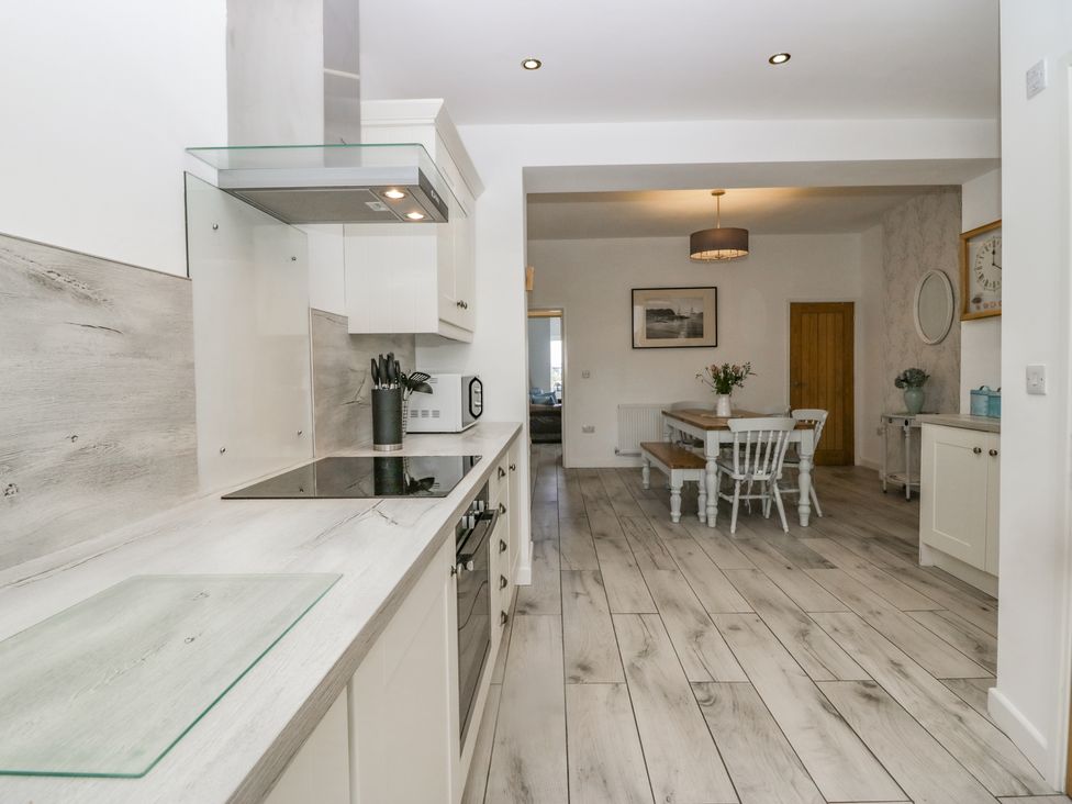 A kitchen with stove and countertop leading to a dining area with table chairs and bench at Driftwood 23 Roa Island in Roa Island