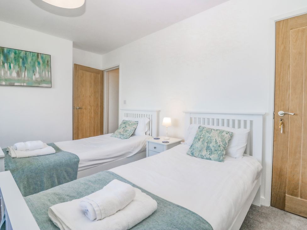 A bedroom with two single beds a nightstand with a lamp between the beds and two wooden doors at Driftwood 23 Roa Island in Roa Island