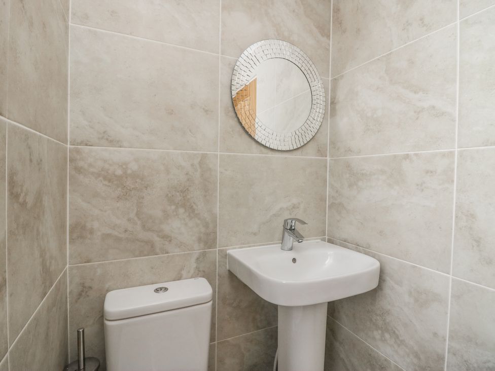 A bathroom with a white toilet a pedestal sink and a round mirror on tiled walls at Driftwood 23 Roa Island in Roa Island