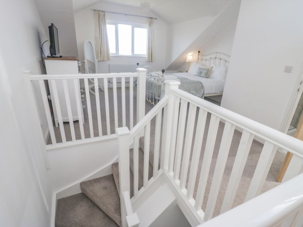 A bedroom with a double bed pillows a bedside lamp a window a dresser with a television and a staircase with white railing at Driftwood 23 Roa Island in Roa Island