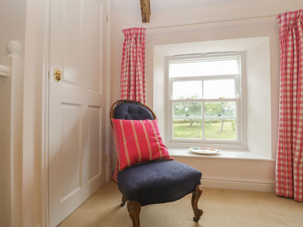 A chair with a pink cushion by a window with checkered pink curtains at Drover's in Sutton Mallet