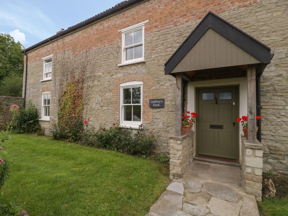 A stone and brick house exterior with a green door and porch at Drover's in Sutton Mallet