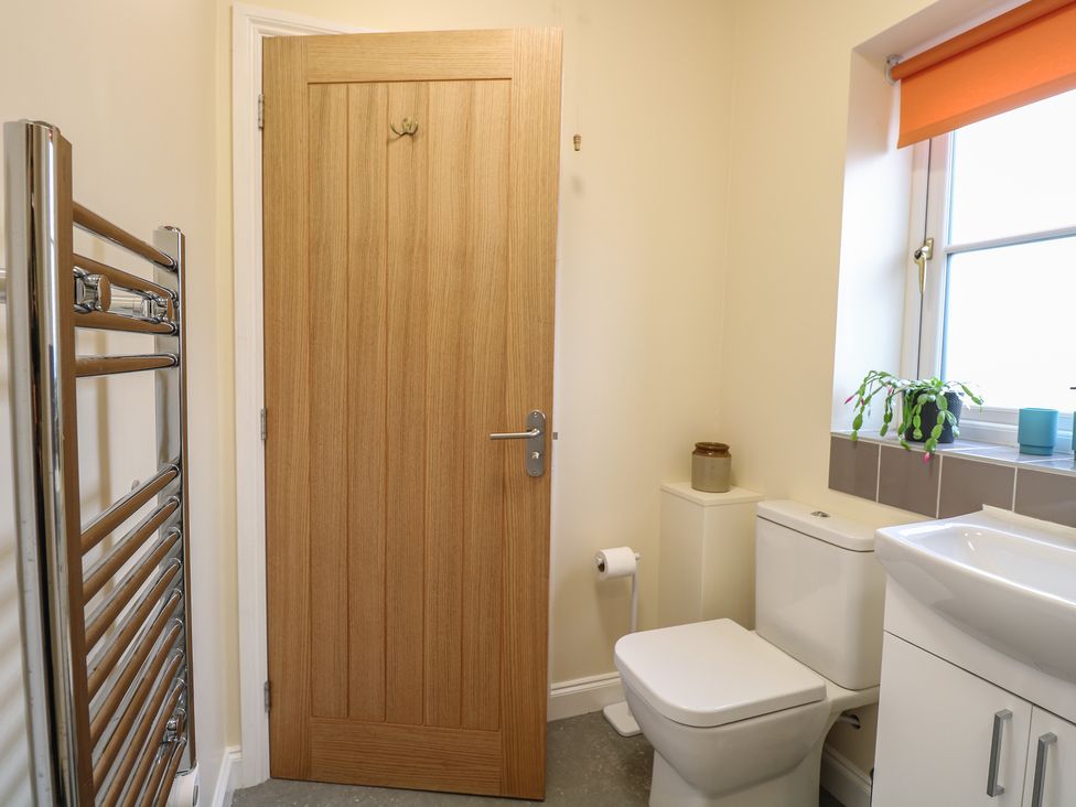A bathroom with a wooden door a white toilet a white sink a towel rack and a window with an orange blind at The Annexe Fulmodestone near Fakenham