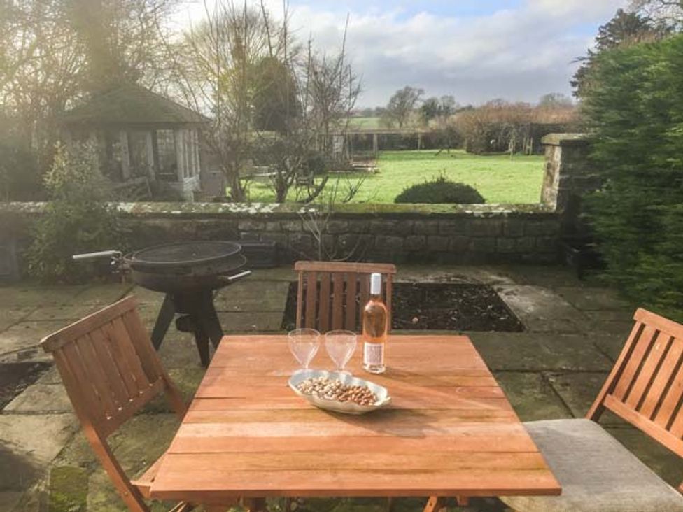 A garden patio with wooden chairs and table with wine and glasses at The Granary in Appleton-le-Moors