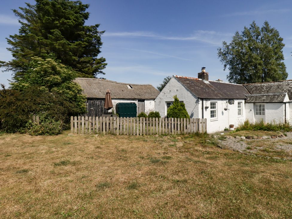 A small white house with a wooden fence and shed in a grassy yard at Camphill in Kirkcudbright