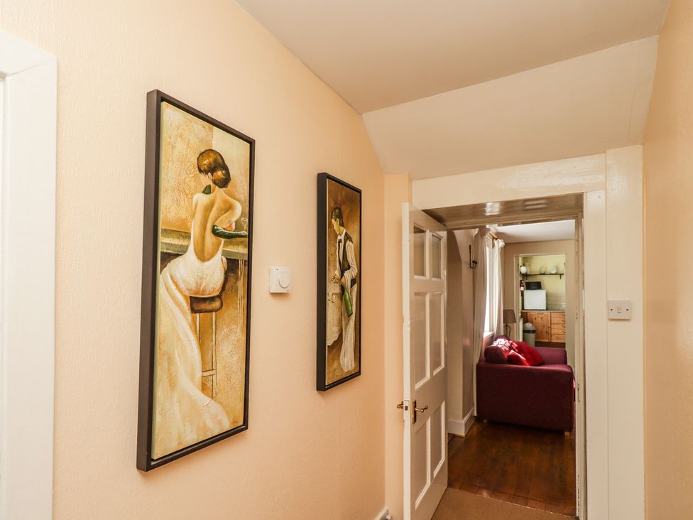 A hallway with two framed paintings on the wall and an open door leading to a room with a red sofa at Camphill in Kirkcudbright