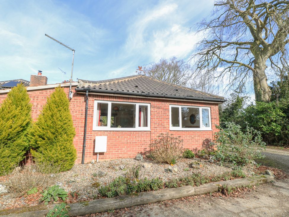 A brick house with two white framed windows and plants in front at The Lodge in Coltishall