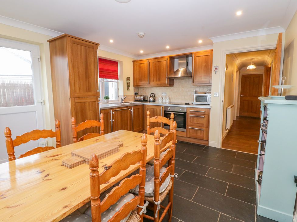 A kitchen with wooden cabinets a dining table with six chairs and a hallway at Llecyn Braf in Amlwch