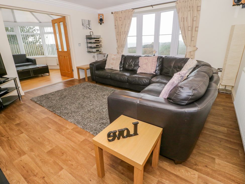 A living room with a black leather corner sofa a wooden side table with Love decoration and a TV at Llewyn Braf in Amlwch