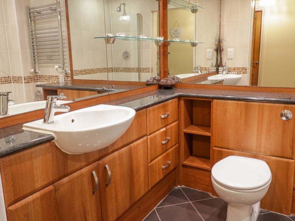 A bathroom with a white sink and toilet wooden cabinets and a large mirror at Llecn Braf in Amlwch
