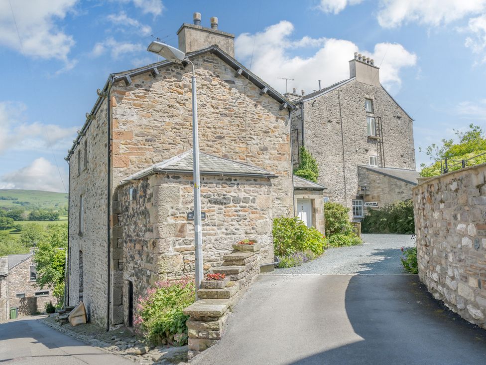 A stone house with a gated driveway and flowers by the entrance at Mill Brow Apartment in Kirkby Lonsdale