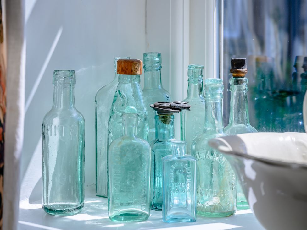 A collection of vintage glass bottles on a windowsill with some cork stoppers and a white ceramic container at Mill Brow Apartment in Kirkby Lonsdale