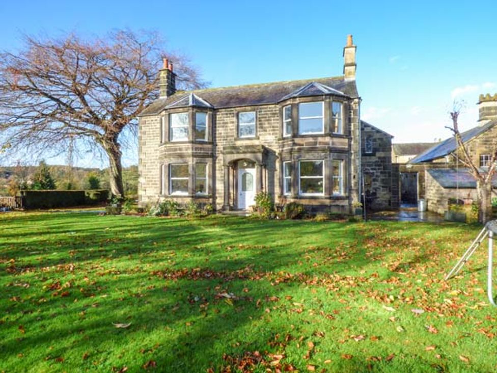 A stone house with bay windows and a lawn with scattered leaves and a large tree at Old Farm House in Rowsley near Bakewell