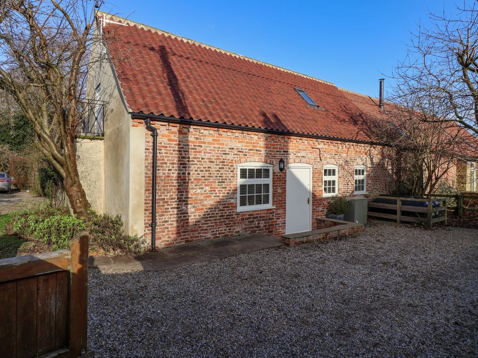 A brick house with a red tiled roof white door and windows with trees around at The Dower House Cottage in Kirklington