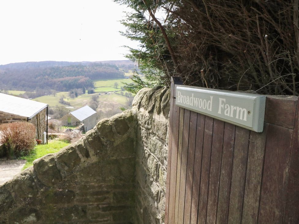 A wooden gate with a sign reading Broadwood Farm next to a stone wall overlooking fields and hills at Broadwood Farm in Hathersage