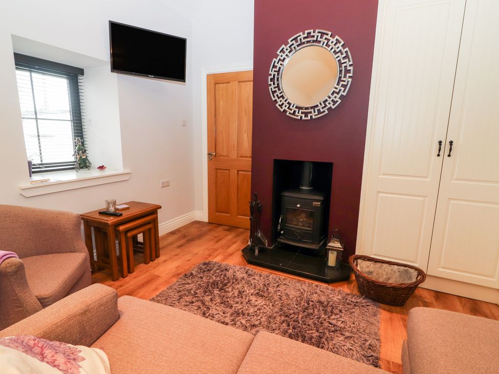 A living room with a wood stove under a circular mirror and a television on the wall at Laharn Cottage in Killorglin County Kerry