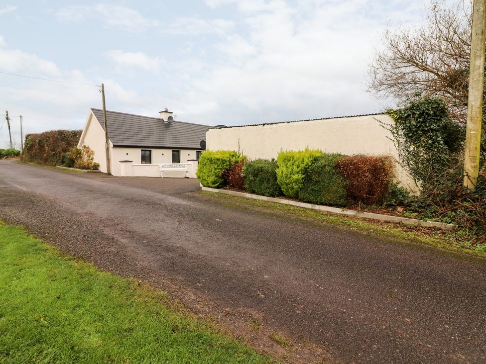 A driveway leading to a single-story house with a slate roof and a white bench outside at Laharn Cottage in Killorglin County Kerry