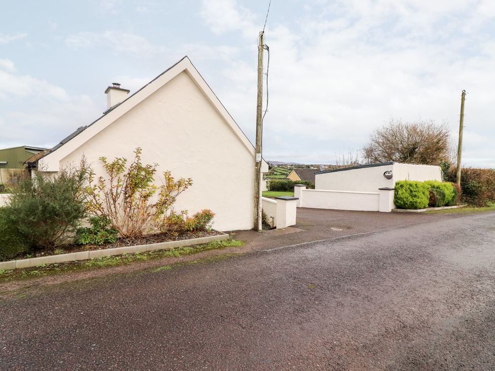 A white house with garden plants and a paved road in front at Laharn Cottage in Killorglin County Kerry