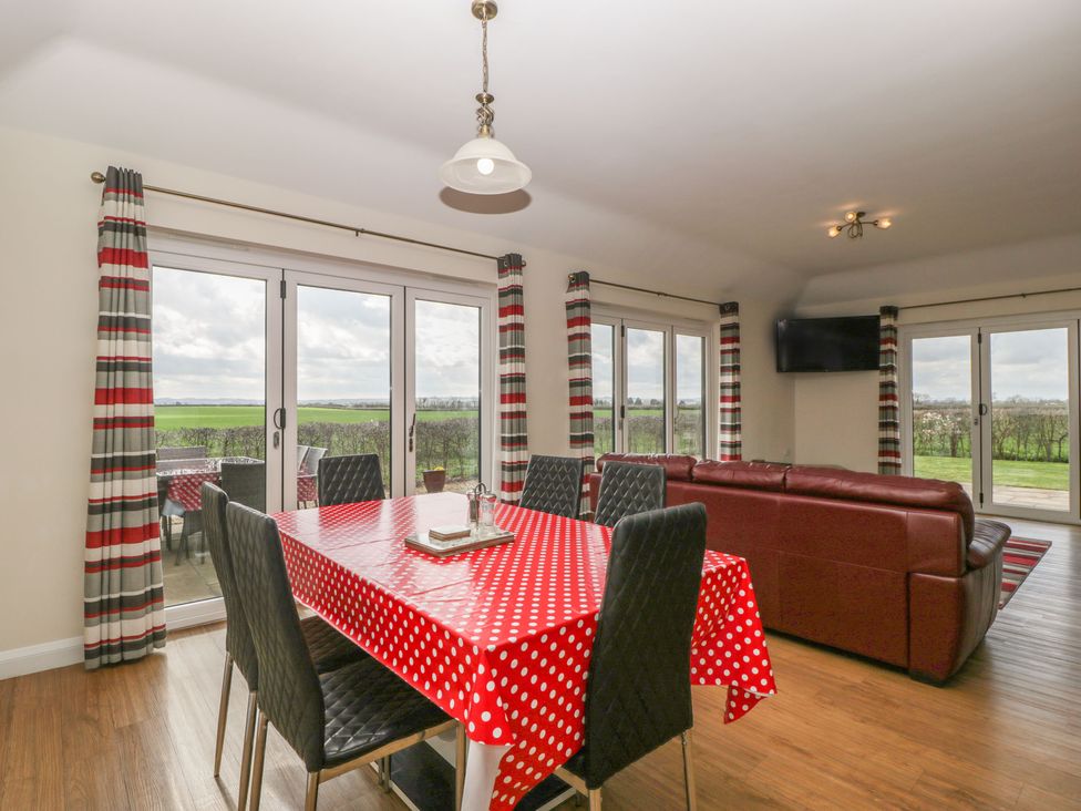 A dining table with red polka dot tablecloth and black chairs next to a brown leather sofa in a room with large glass doors at Rectory Farm View Queen Camel near Yeovil