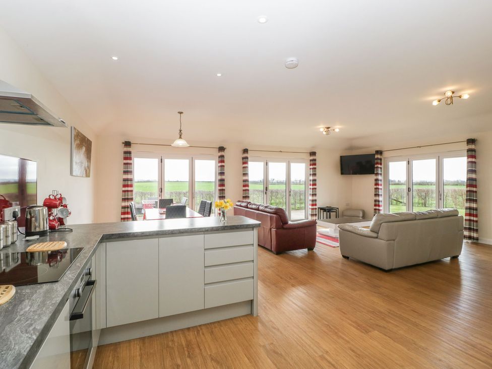 An open plan kitchen and living area with sofas dining table and large windows showing outside view at Rectory Farm View in Queen Camel near Yeovil