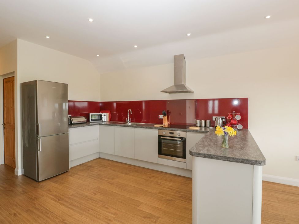 A kitchen with a stainless steel refrigerator oven red backsplash and flowers on the counter at Rectory Farm View Queen Camel near Yeovil