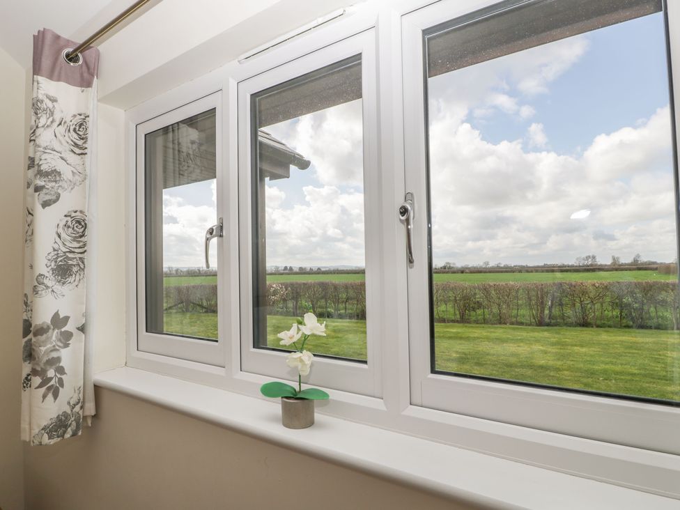 A window with white frames and floral curtains overlooking a grassy field at Rectory Farm View in Queen Camel near Yeovil