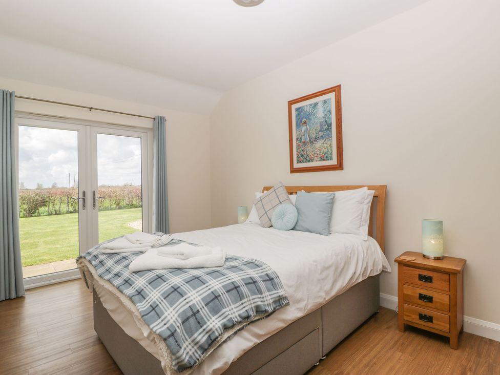 A bedroom with bed and pillows bedside table and lamp and glass doors overlooking a garden at Rectory Farm View in Queen Camel near Yeovil