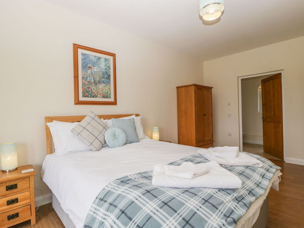 A bedroom with a bed pillows and folded towels on a checked blanket a wooden wardrobe and a bedside table with a lamp at Rectory Farm View Queen Camel near Yeovil