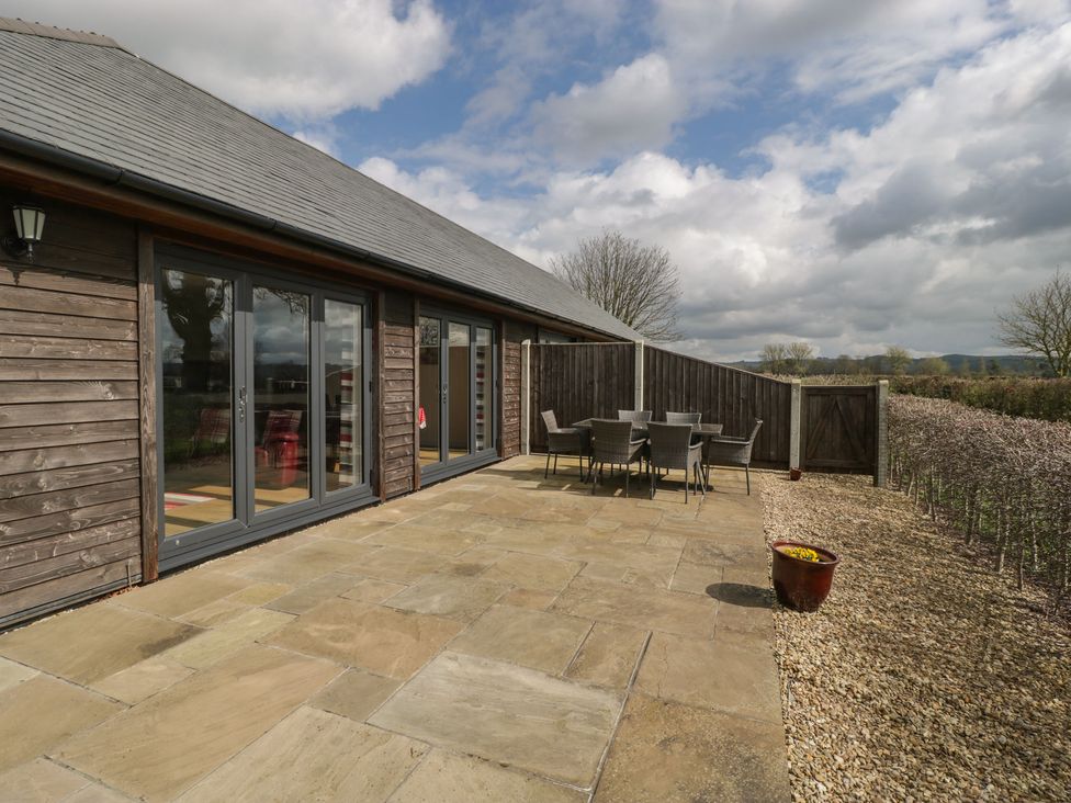 An outdoor patio area with stone tiles a dining table with chairs wooden fence and gate at Rectory Farm View in Queen Camel near Yeovil