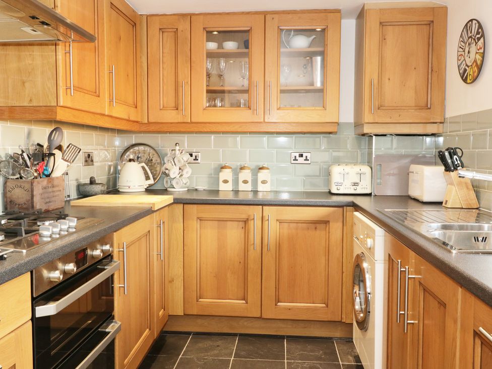 A kitchen with wooden cabinets a gas stove a kettle a toaster and a washing machine at Llwyn Onn Dolwyddelan