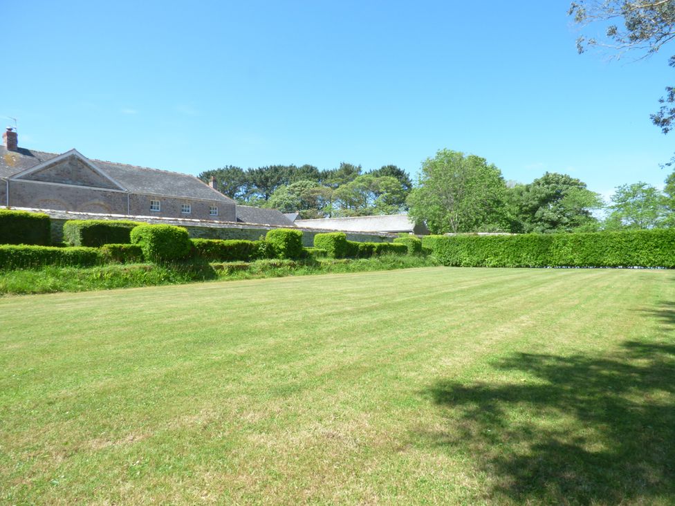 A large lawn with trimmed hedges and trees near a stone building at Parlour Cottage in Marazion