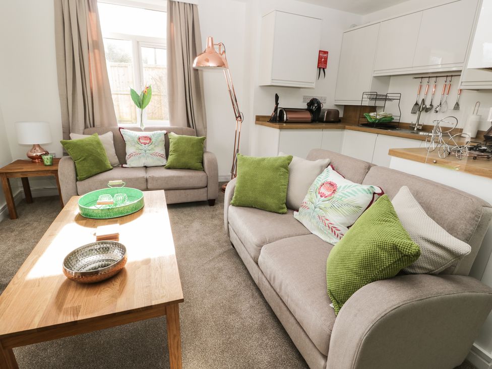 A living room with beige sofas and green cushions next to a kitchen area at Manor Heath Apartment 1 in Scarborough