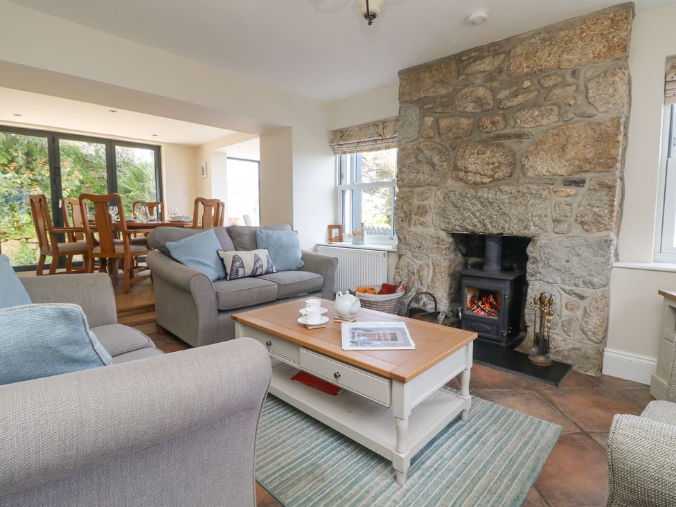 A living room with sofas coffee table and a stone fireplace adjacent to a dining area with wooden chairs and table at Rose Villa in Newlyn
