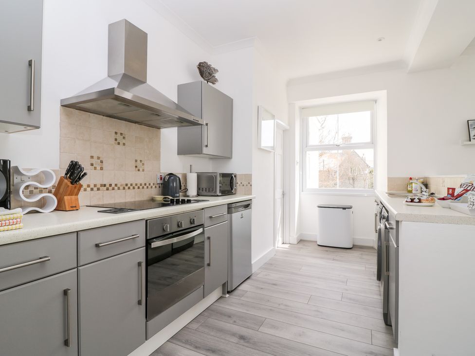 A kitchen with grey cabinets appliances a window and a tiled backsplash at Sea Breeze in Marazion