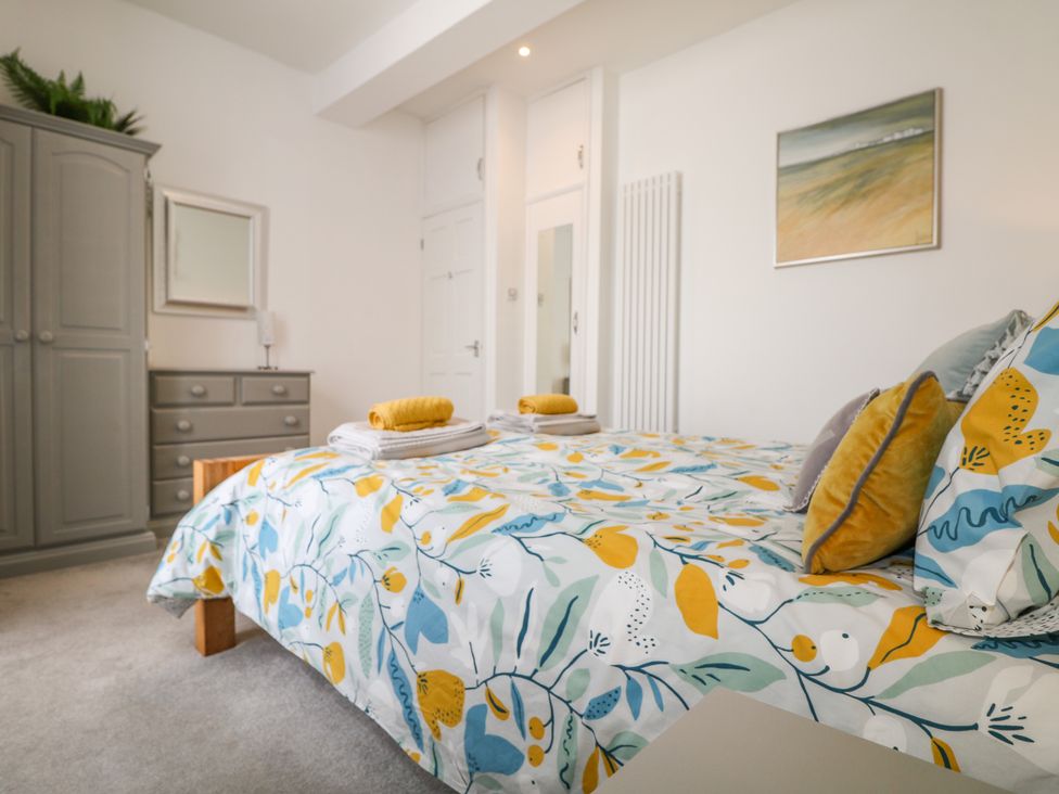 A bedroom with a bed covered with floral bedding and folded towels next to a wardrobe and dresser with a mirror at Sea Breeze in Marazion