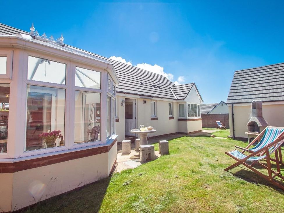 A backyard with a patio table and stools a conservatory and deck chairs at Fairways in Woolacombe