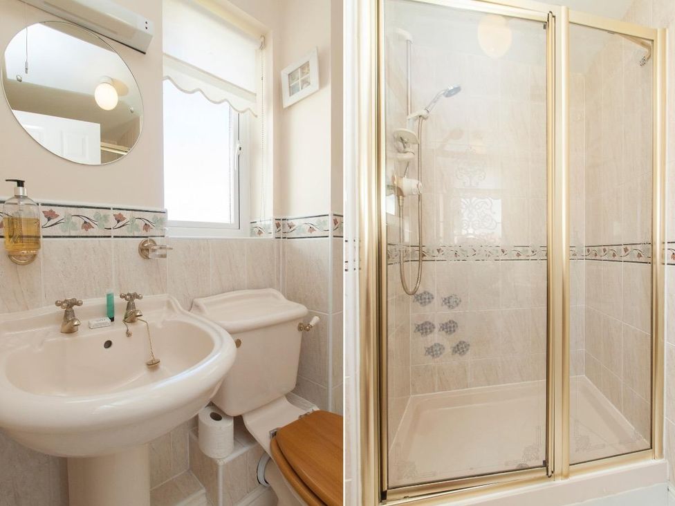 A bathroom with a sink mirror toilet with wooden seat and a shower with glass doors at Fairways in Woolacombe