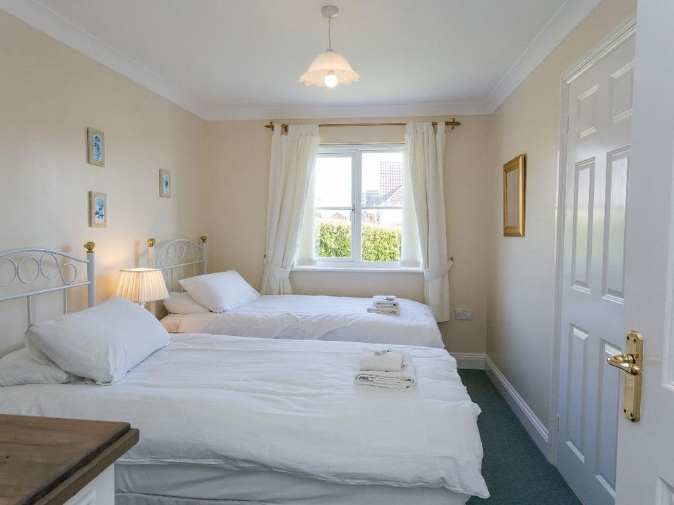 A bedroom with two single beds white bedding and a window with white curtains at Fairways in Woolacombe
