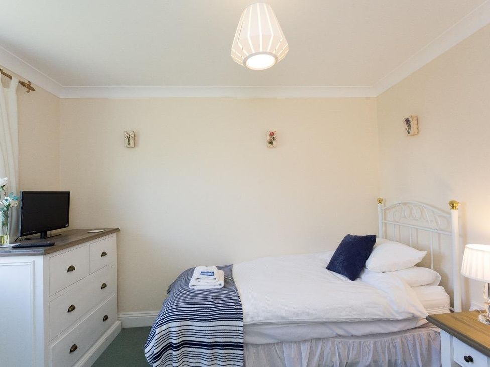 A bedroom with a single bed a blue and white striped blanket a chest of drawers with a television and a lamp on a bedside table at Fairways in Woolacombe